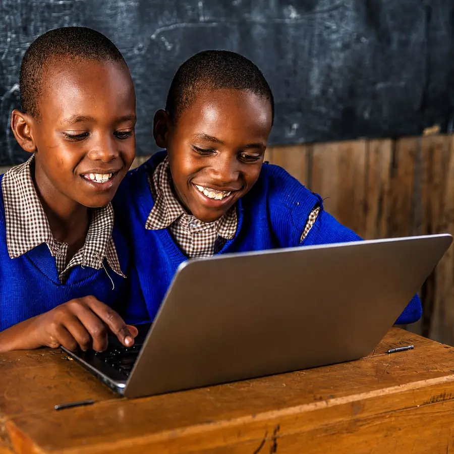 Two learners in blue school jumpers smiling at a laptop